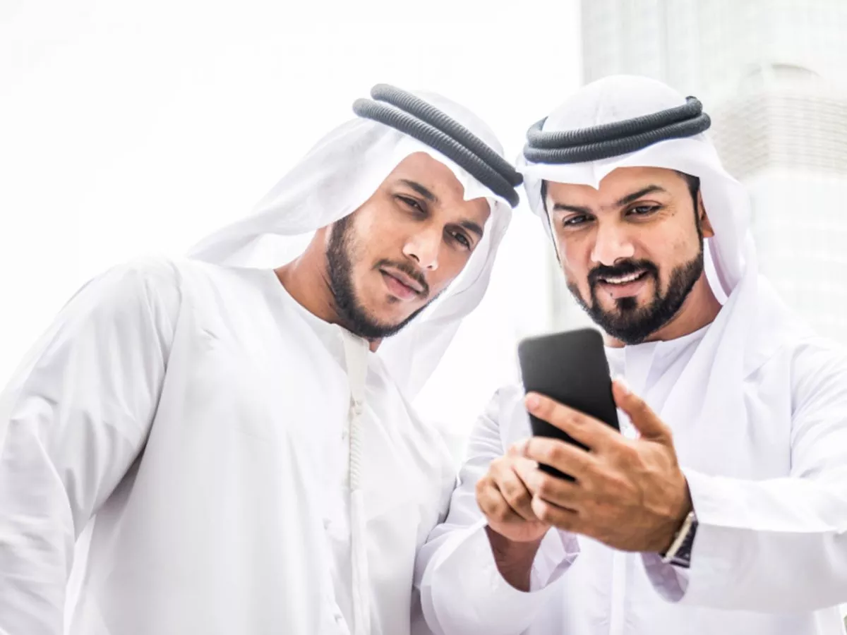 Image of two Emirati nationals looking at a phone and engaged in discussion. They appear happy and enthusiastic, with an emphasis on the phone screen.